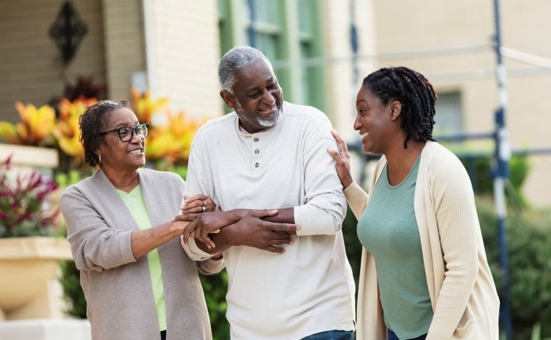 Daughter walking outdoors with an older couple while offering support
